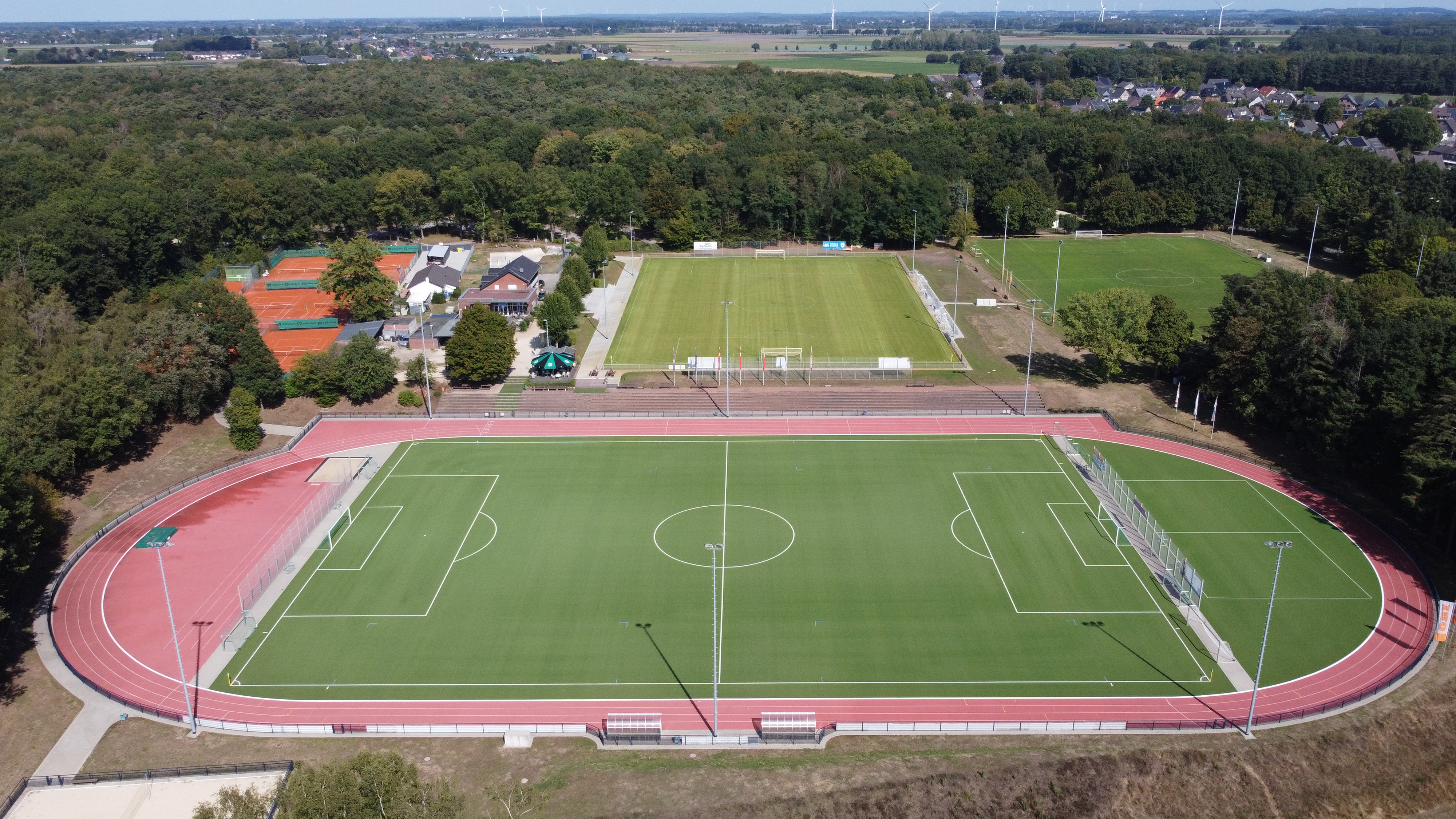 Luftbild Sportanlage Am Vennberg, im Vordergrund Kunstrasenplatz mit Laufbahn und Strahlern, im Hintergrund zwei Fußballrasenplätze, Vereinsheim, Tennisplatz, niedrige Waldzonen, Feld- und Gebäudelandschaft